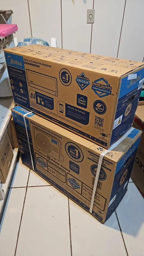 Duas caixas empilhadas de ar-condicionado Midea Série AI Ecomaster Inversor (unidades interna e externa) sobre piso cerâmico claro