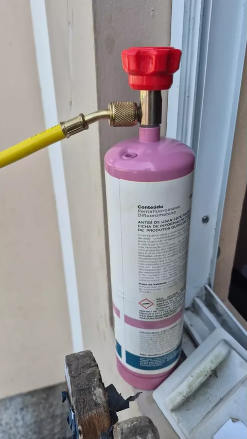 Cilindro rosa de refrigerante R-410A com mangueira amarela conectada à válvula, em serviço de carga ou diagnóstico